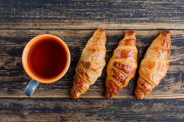 Croissant with cup of tea on wooden table, flat lay.