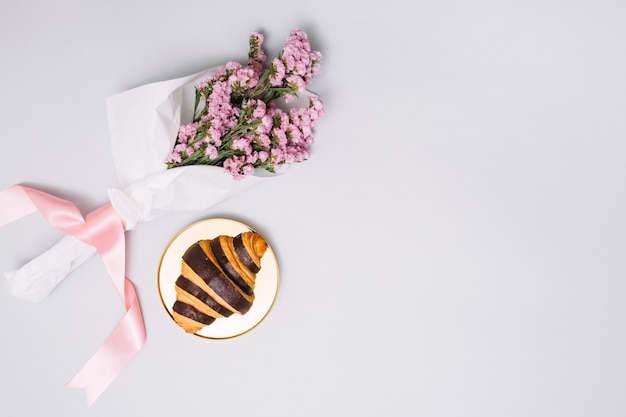 Foto gratuita croissant con bouquet di fiori sul tavolo