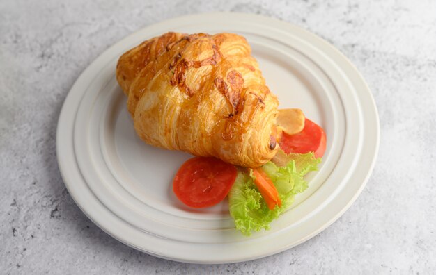 Croissant with hot dog on white dish