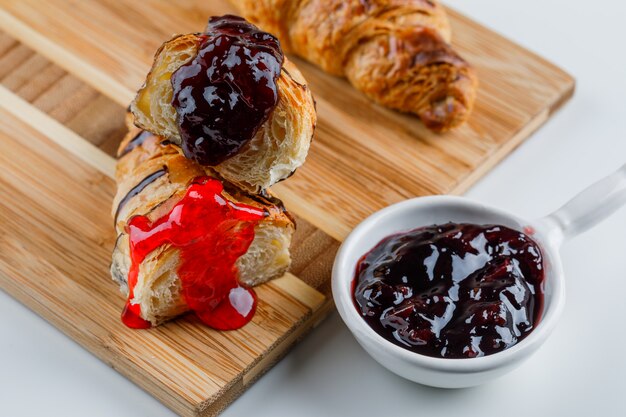 Croissant with jam on white and cutting board, high angle view.
