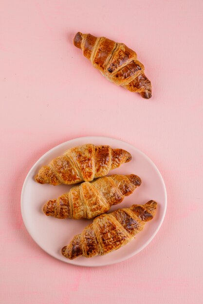 Free photo croissants in a plate on pink table, flat lay.