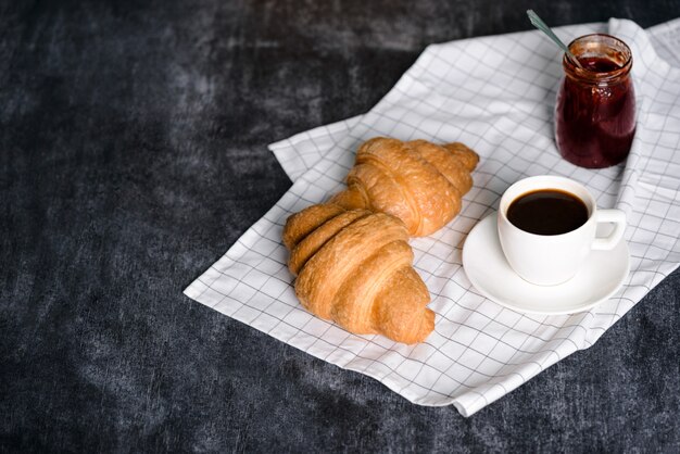  croissants, pot with jam and coffee cup aside on grey table