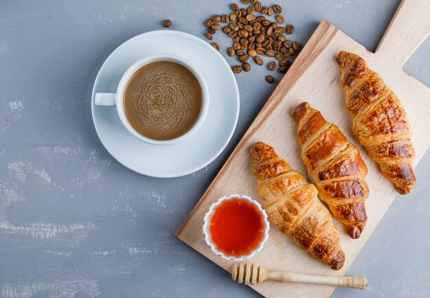 Croissants with coffee and beans, honey, dipper on plaster and cutting board, flat lay.