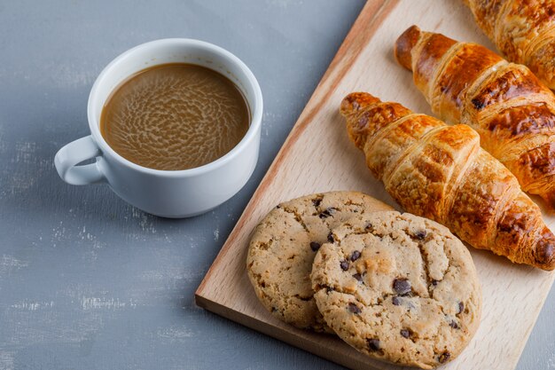 Croissants with cup of coffee, cookies high angle view on plaster and cutting board
