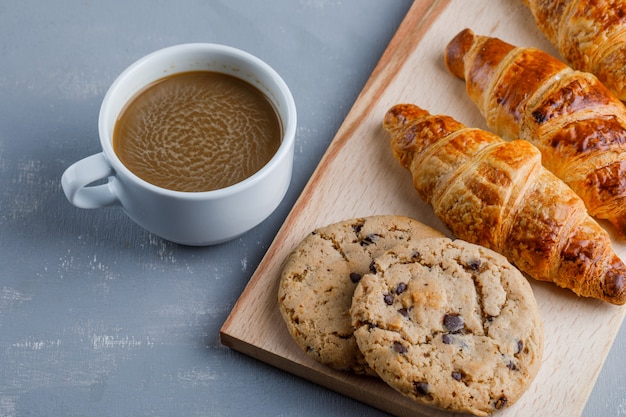 一杯のコーヒー、クッキーと石膏とまな板の上の高角度のビューのクロワッサン