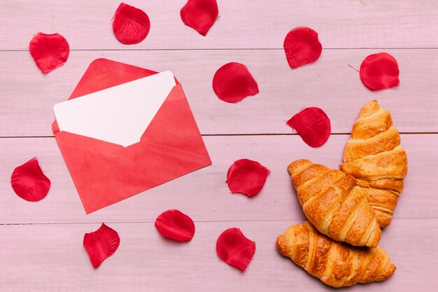 Croissants with red roses petals and envelope