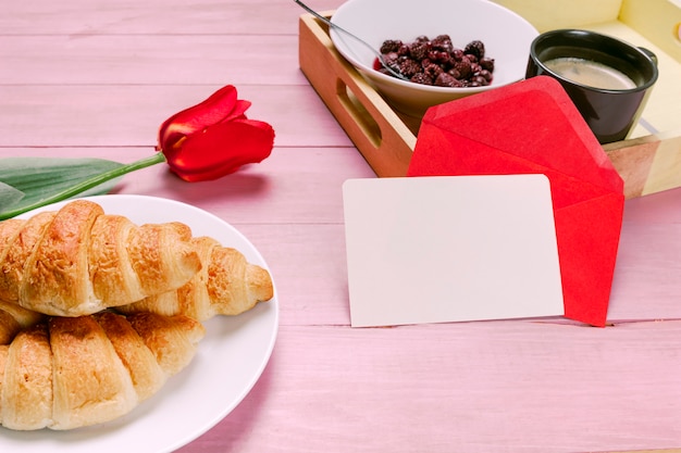 Free photo croissants with red tulip and blank paper