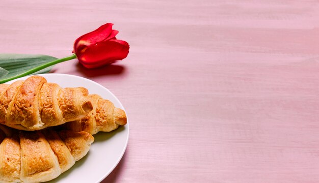 Croissants with red tulip on table