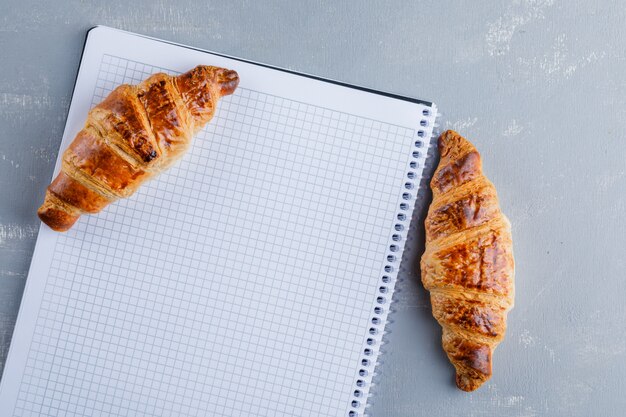 Croissants with spiral notebook, flat lay.