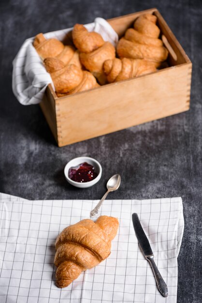  croissants in wooden box and jam pot aside on grey table