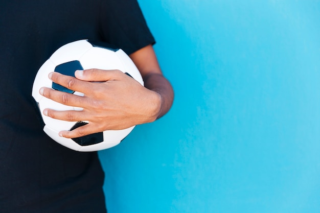Crop of arm holding soccer ball near wall