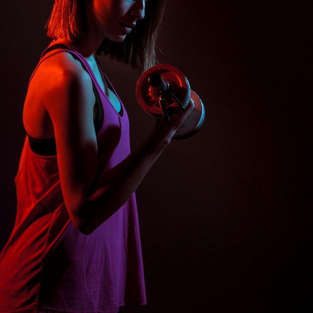 Crop athletic woman training bicep in dark