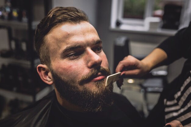 Crop barber combing beard of man