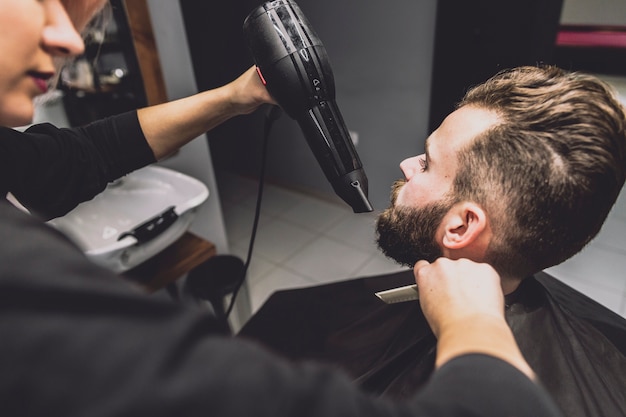 Crop barber drying beard of customer