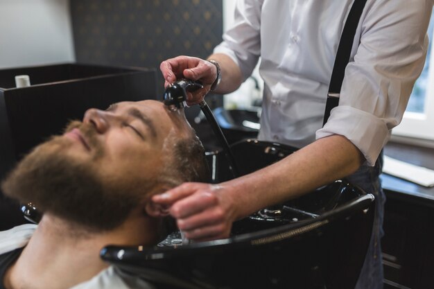 Crop barber washing hair of bearded man