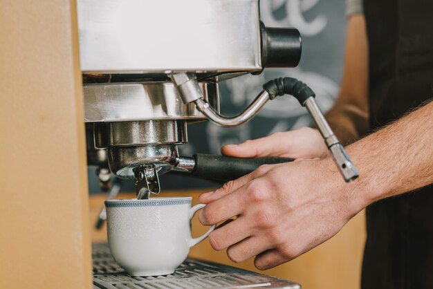 Crop barista ouring coffee