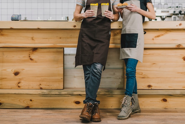 Crop baristas with cups and pastry