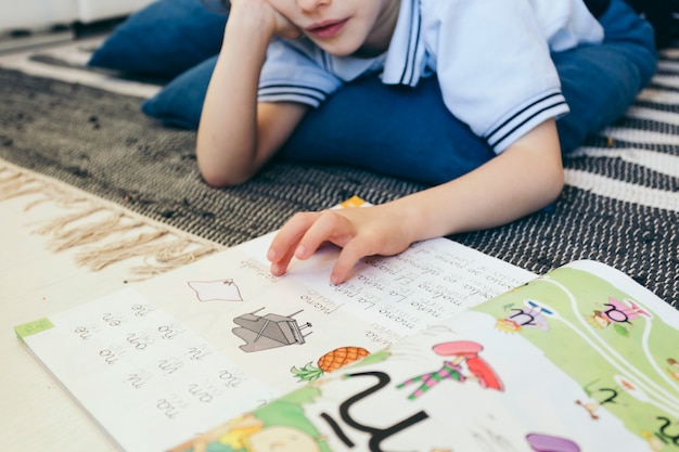 Crop boy reading textbook on floor