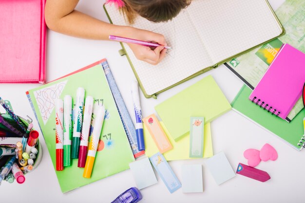 Crop child at table with school supplies