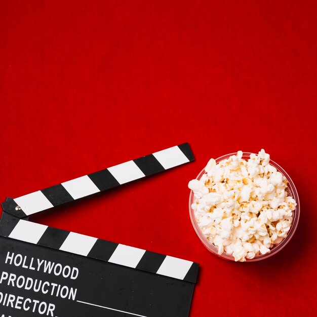 Crop clapperboard and popcorn in plastic cup