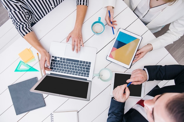 Crop coworkers using modern devices at desk