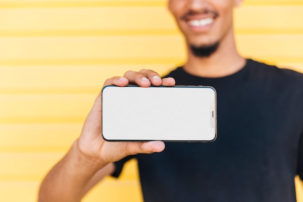 Crop ethnic man showing smartphone