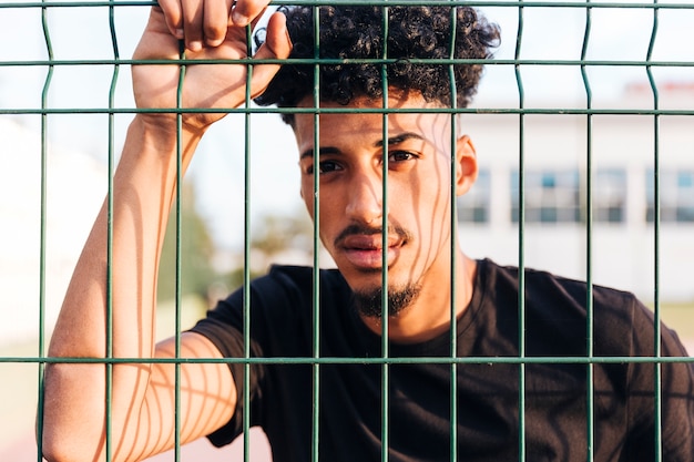 Crop ethnic young man behind fence