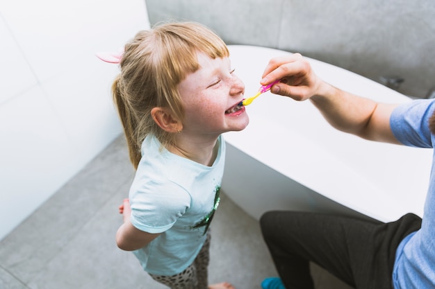 Crop father brushing teeth of daughter