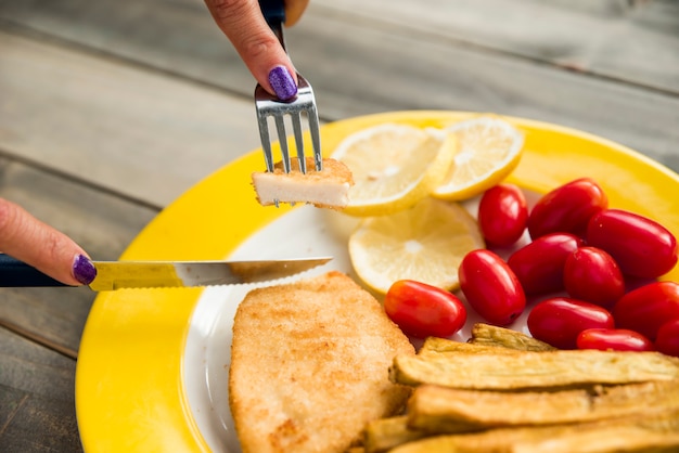 Crop female cutting fried chicken on plate