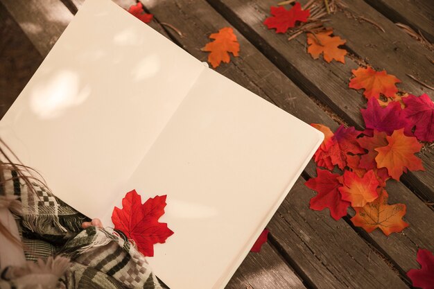 Crop female reading book with autumn leaf