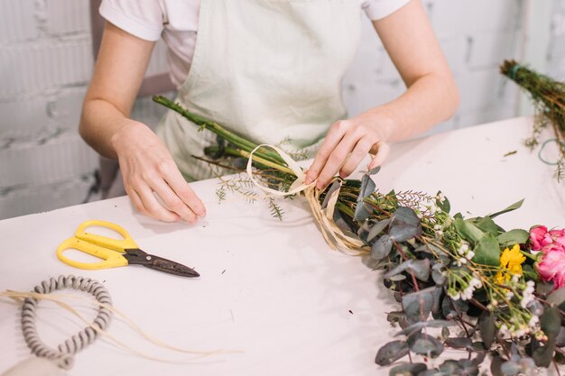 Crop florist attaching ribbon to bouquet