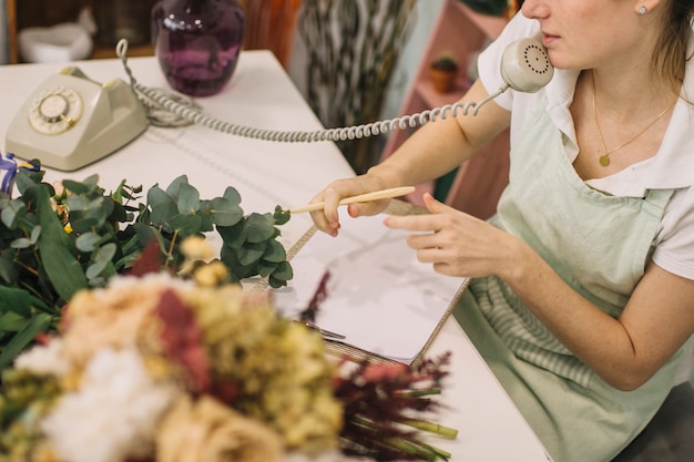 Crop florist making notes during phone conversation