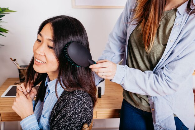 Crop girl helping pretty friend with hairstyle