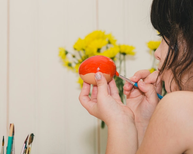 Crop girl painting egg with orange