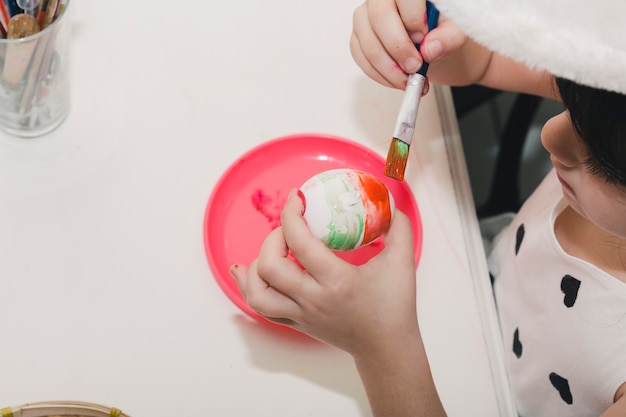 Crop girl painting egg with red