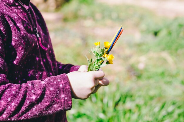 Crop girl with flowers and sticks in field