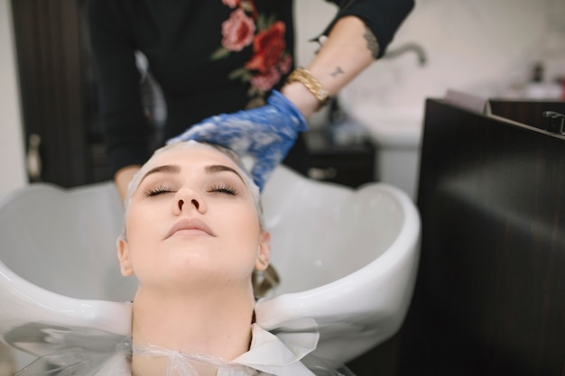 Crop hairdresser washing hair of blonde