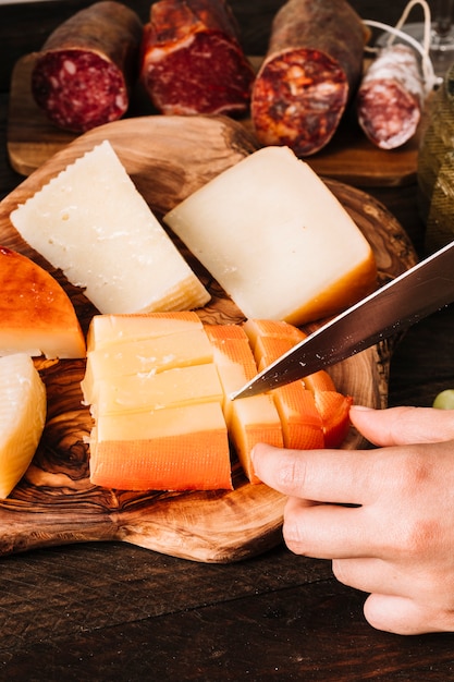 Crop hand cutting cheese near sausages