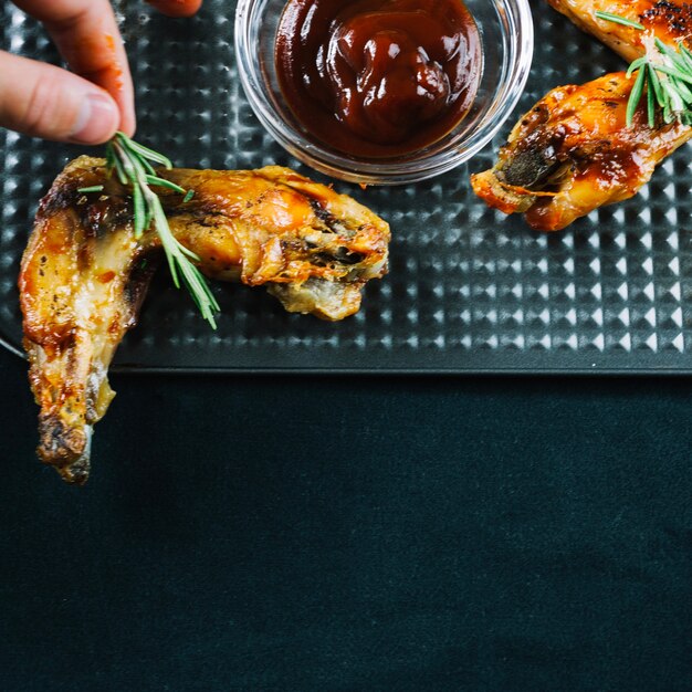 Crop hand decorating chicken wings with rosemary