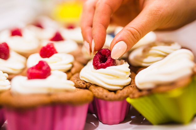 Crop hand decorating muffin with raspberries