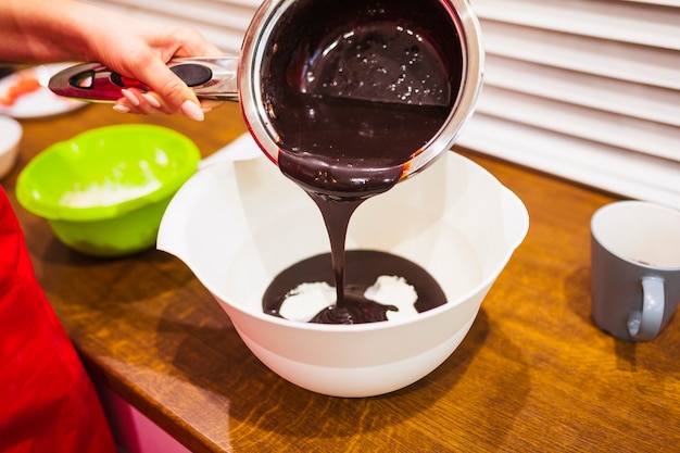 Crop hand filling bowl with chocolate sauce