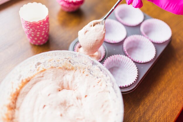 Crop hand filling cups with cupcake batter