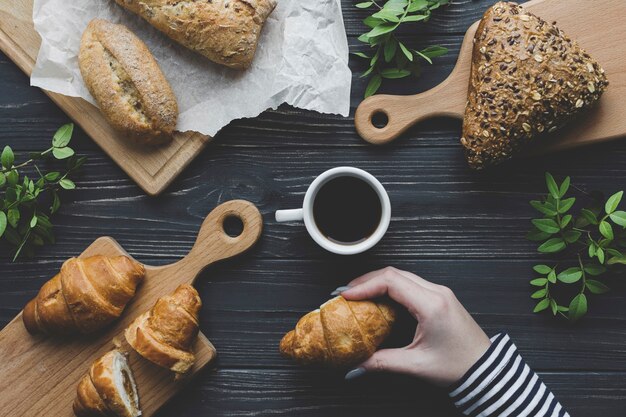 Crop hand holding croissant near coffee