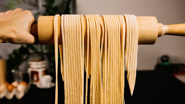 Crop hand holding pasta on rolling pin