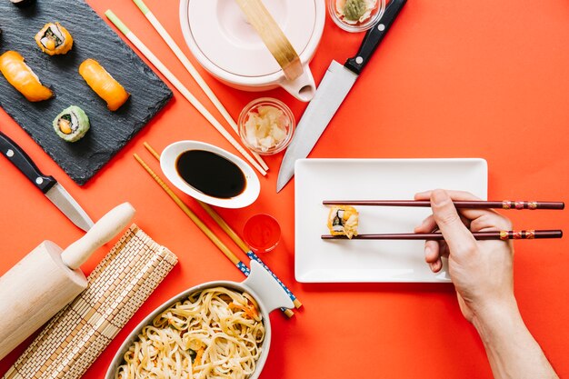 Crop hand holding roll near Japanese food