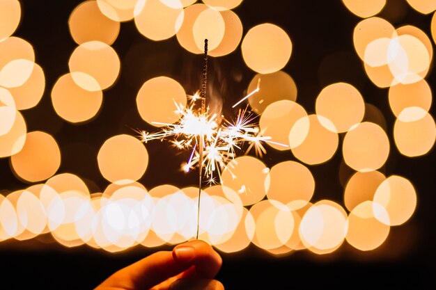 Crop hand holding sparkler near lights