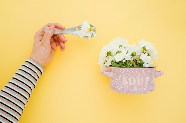 Crop hand near saucepan with flowers