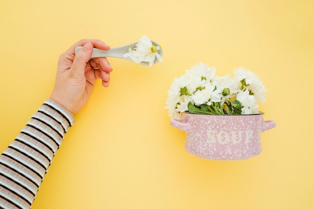Crop hand near saucepan with flowers