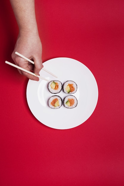 Foto gratuita raccolga i sushi di raccolto della mano su fondo rosso