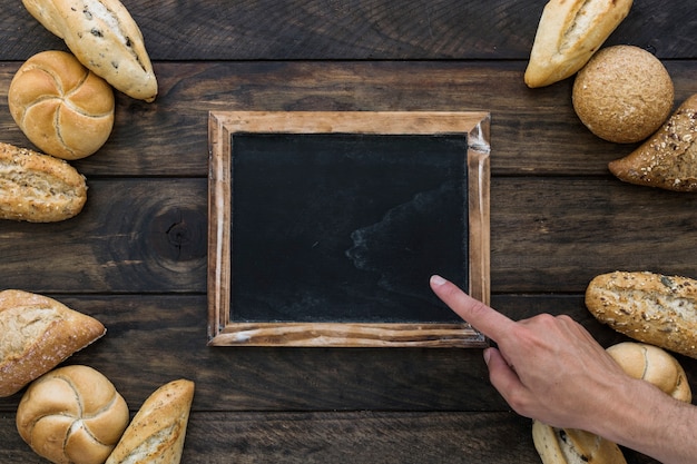 Crop hand pointing at blackboard near bread